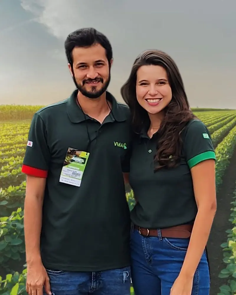 Khiara Campos e o marido Bruno em pé lado a lado num campo de soja verde, sorrindo em uniforme de expositor.
