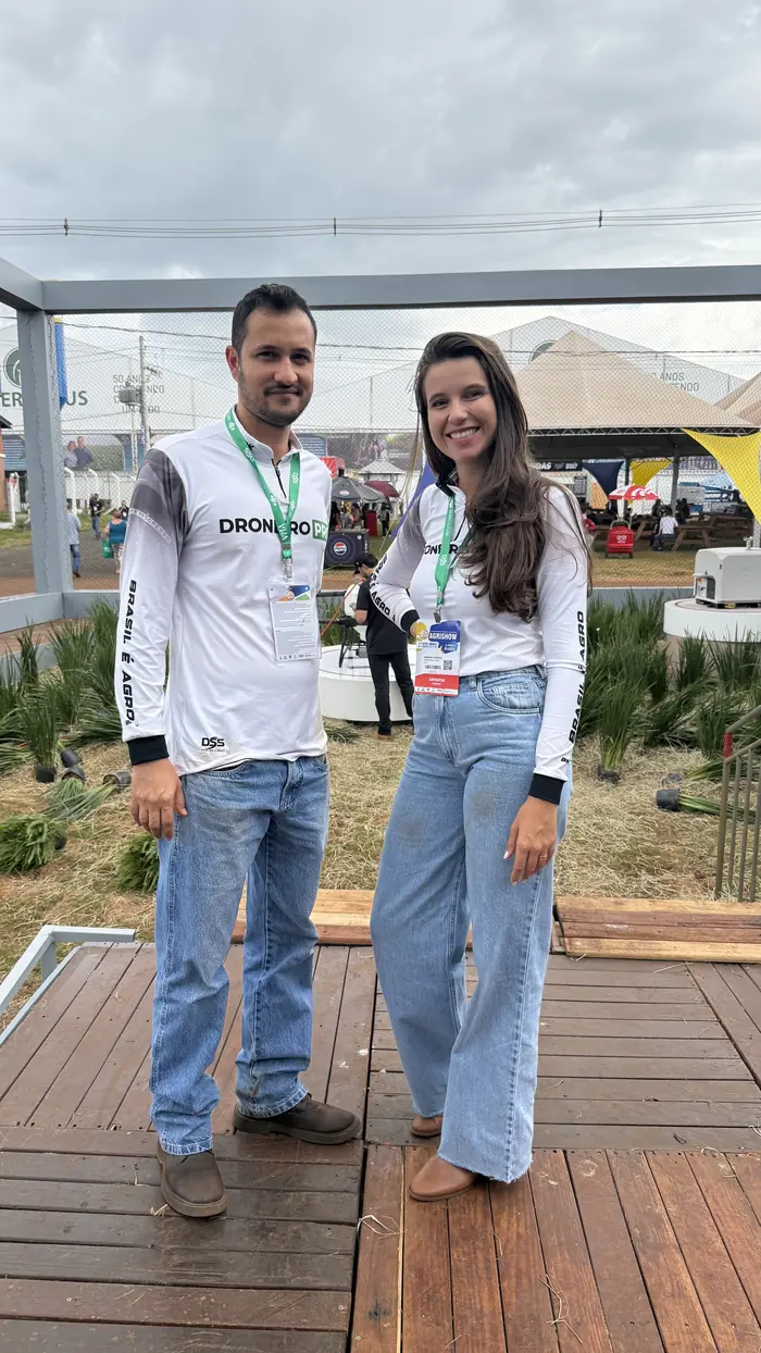 Khiara e Bruno posando no estande do Drone Sem Segredos durante a Agrishow, com crachá de expositor.