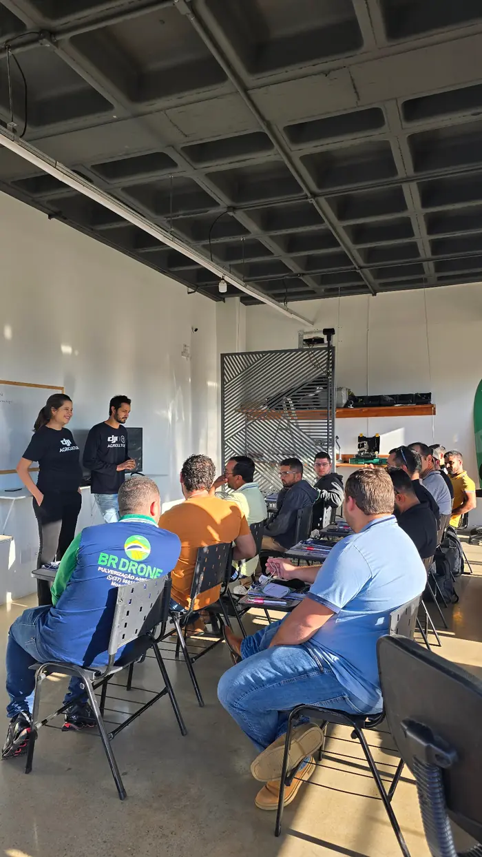 Khiara e Bruno ministrando aula presencial de drone agrícola para pilotos sentados em uma turma cheia.